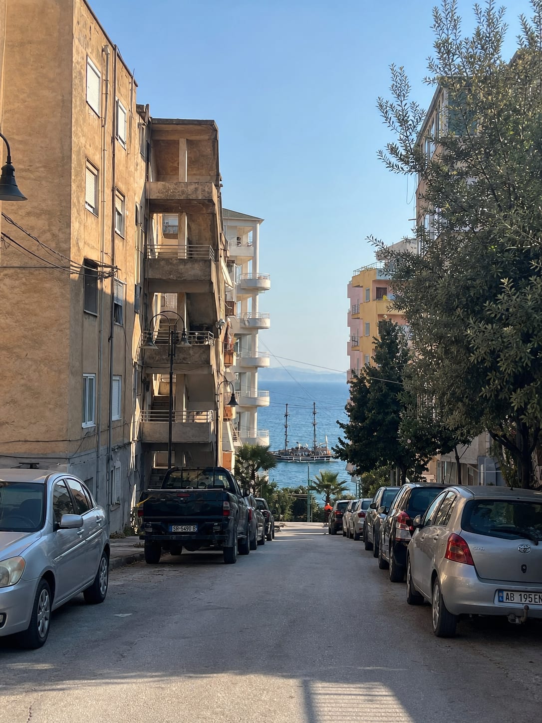 Narrow street in Sarandë with cars parked along both sides.